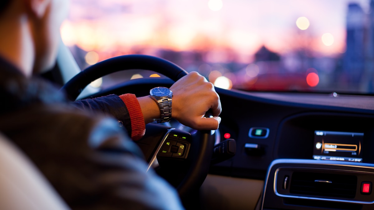 Řidič držící volant při jízdě městem za soumraku